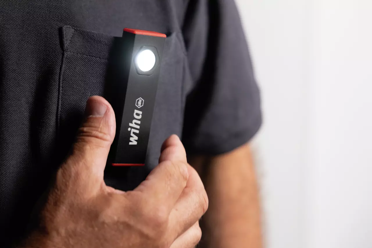 A person holding a small black flashlight with a clip near a shirt pocket.
