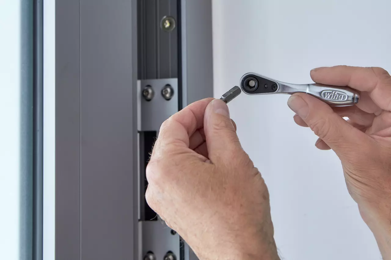A person using a small ratchet wrench near a metal frame