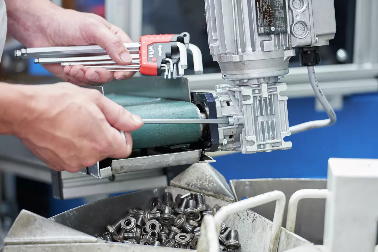 Person using a hex key set on a machine with bolts in the foreground.
