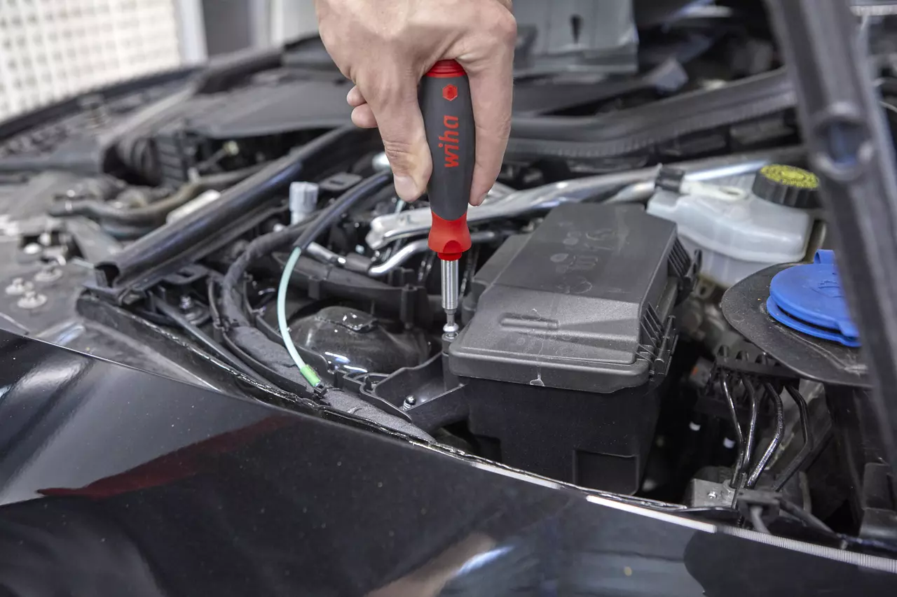 Person using a screwdriver on a car engine part.