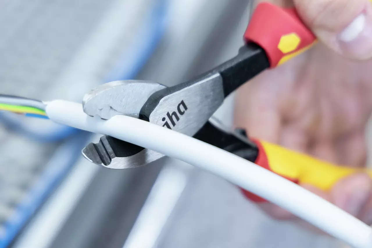 Person using pliers to cut a white cable.