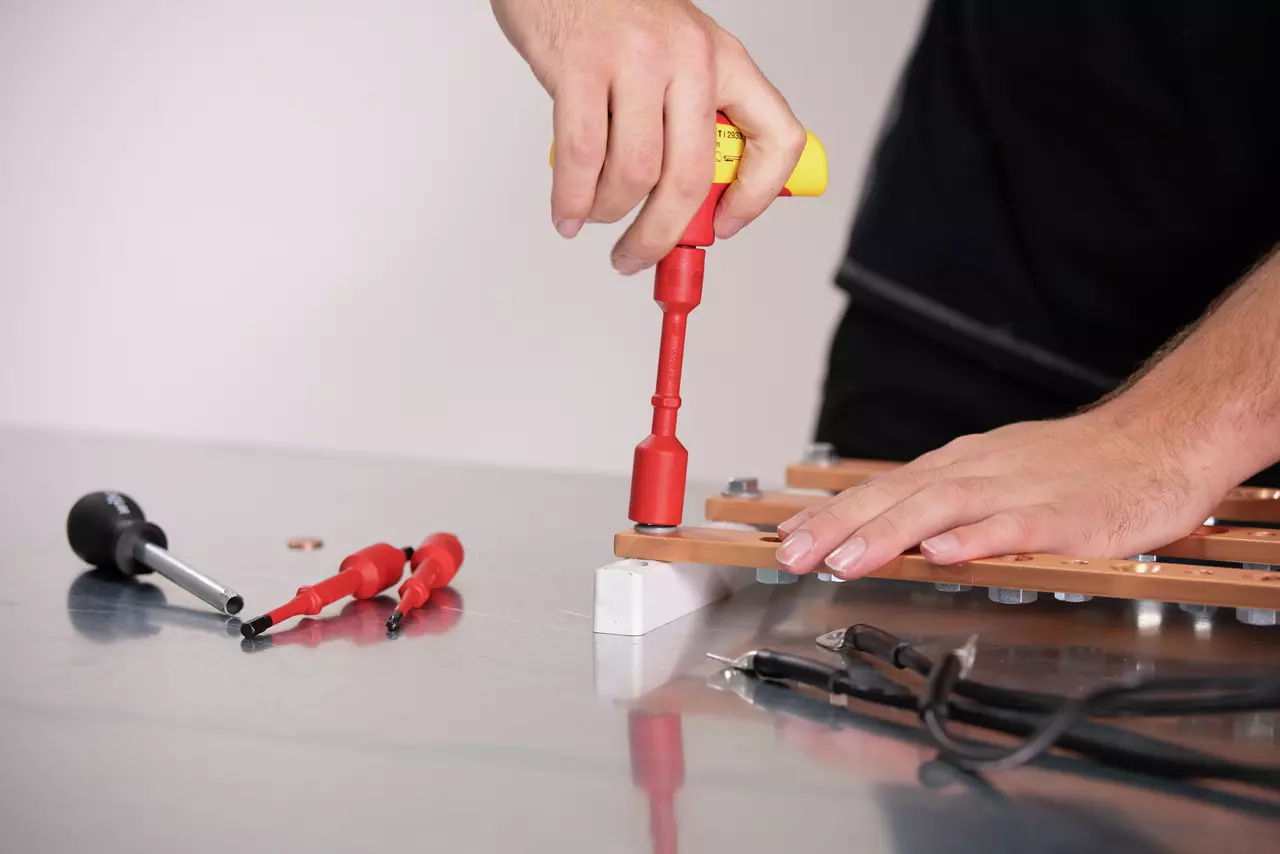 Person using an electric screwdriver on a metal component, with tools on a table.