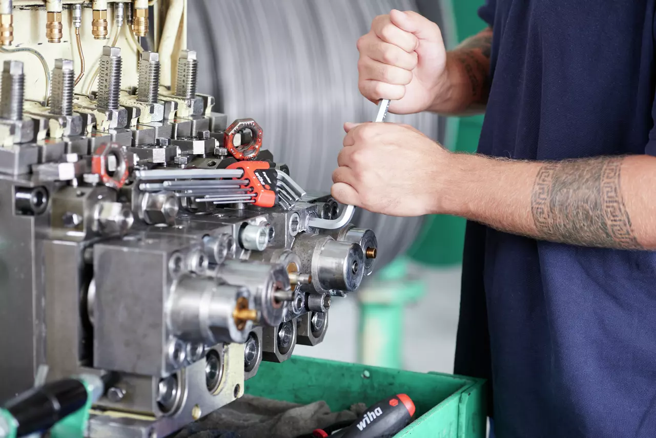Person using a wrench on industrial machinery with tools nearby.