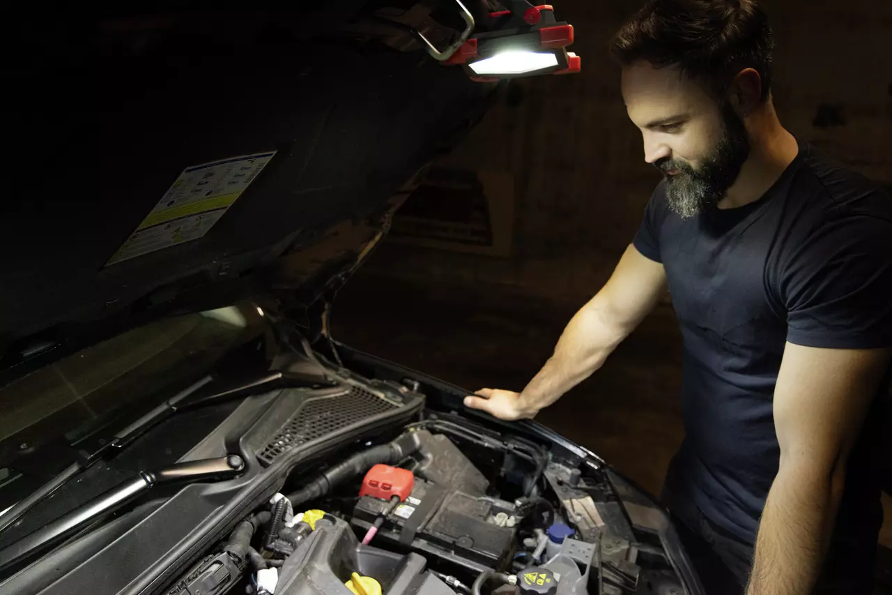 Person inspecting car engine bay with hood open and light.