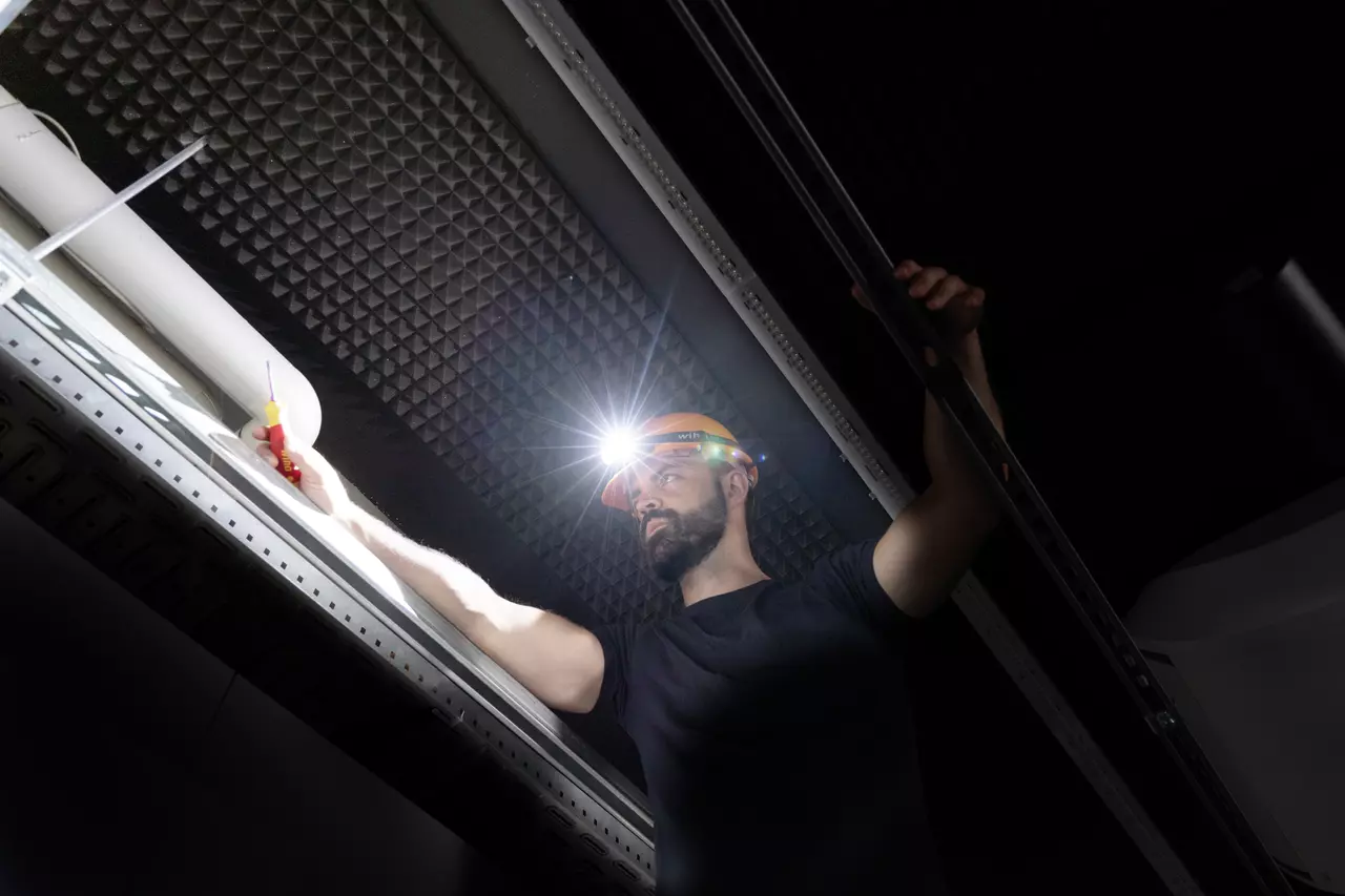 Person wearing a headlamp working on a ceiling with a screwdriver.