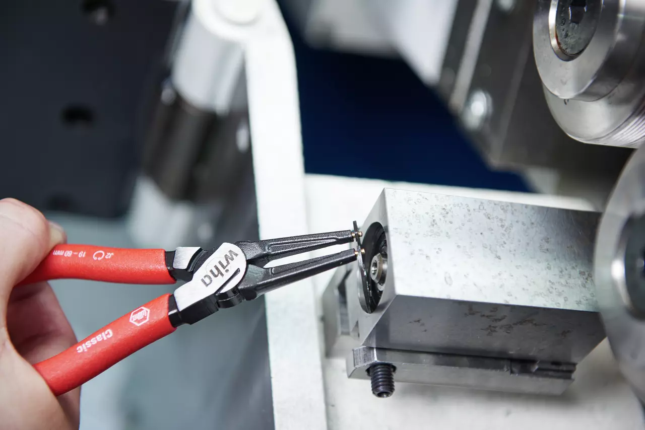 A person uses snap ring pliers to adjust a metal component.