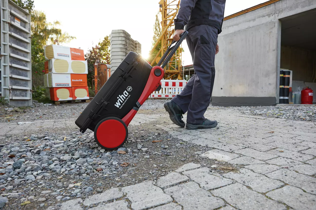 Person pulling a tool case with red wheels on a rough outdoor surface.
