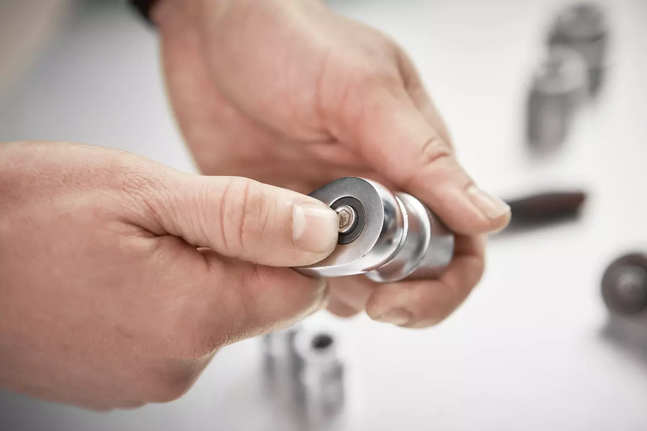 A person holding a small metallic tool with a hexagonal socket in their hands.