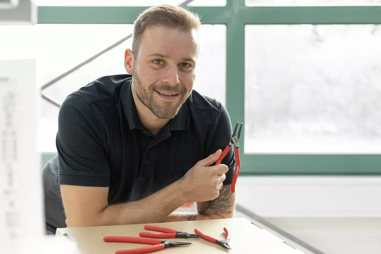 A person holding red-handled pliers, with more pliers on the table