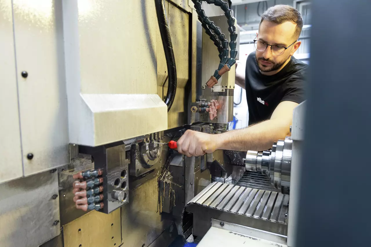 A person using a red-handled tool on a CNC machine in a workshop.