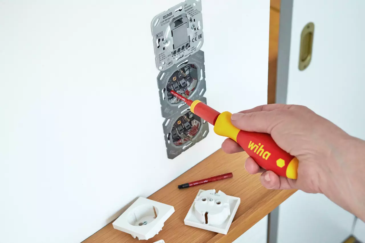 Person installing socket with electric screwdriver on wall.