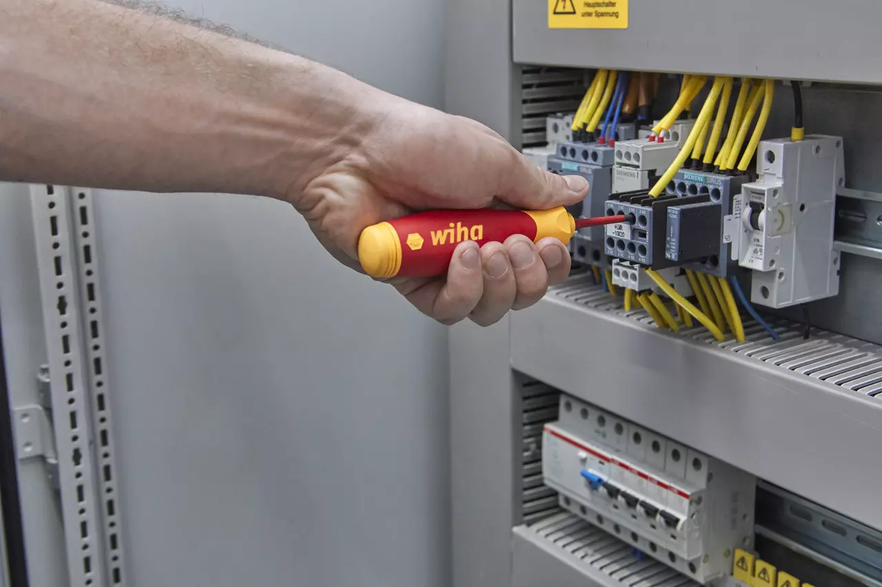 Hand using an electric screwdriver on an electrical panel with yellow wires.