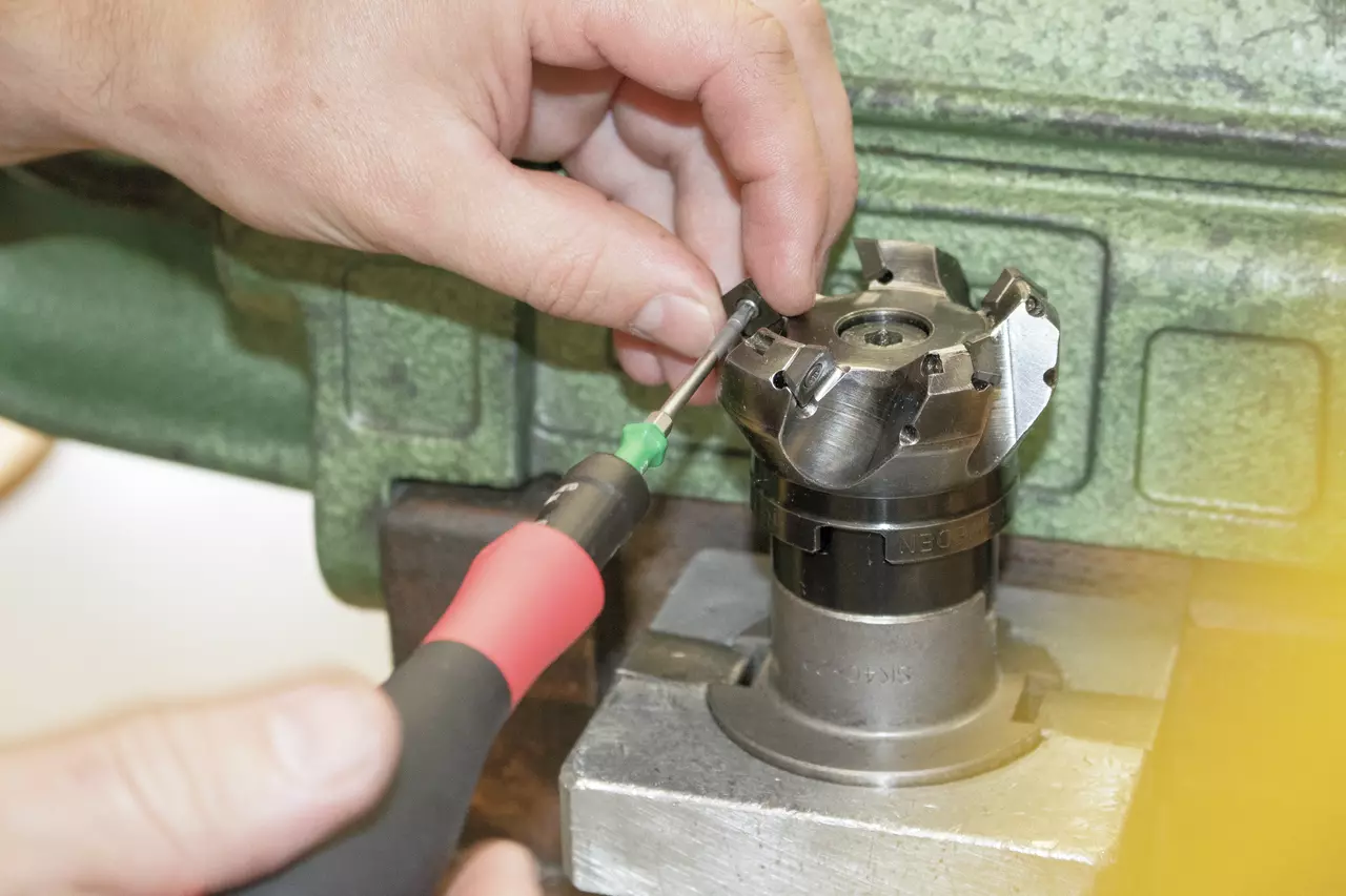 Hands using a screwdriver on a metal cutting tool in a workshop setting.