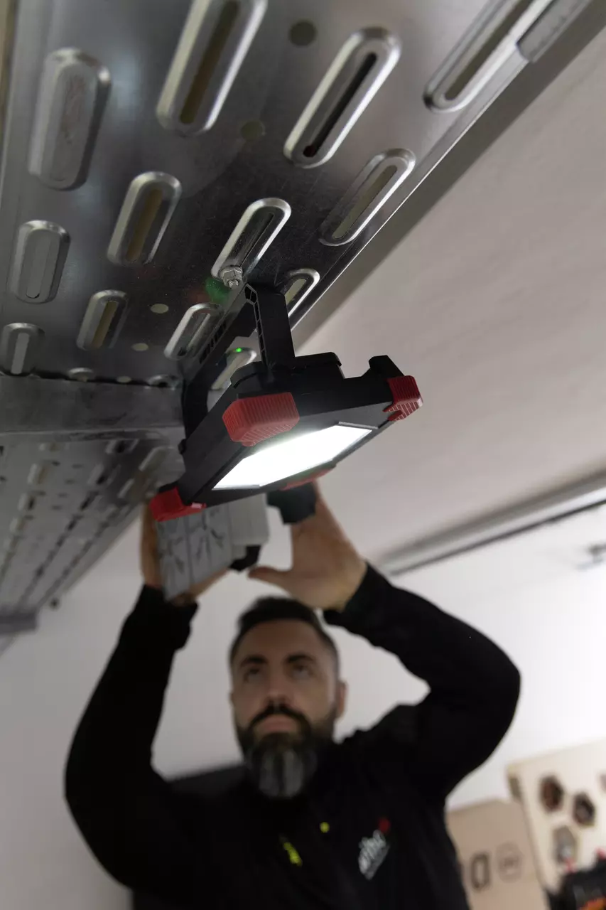 A person mounting a floodlight with magnets on a metal ceiling structure.
