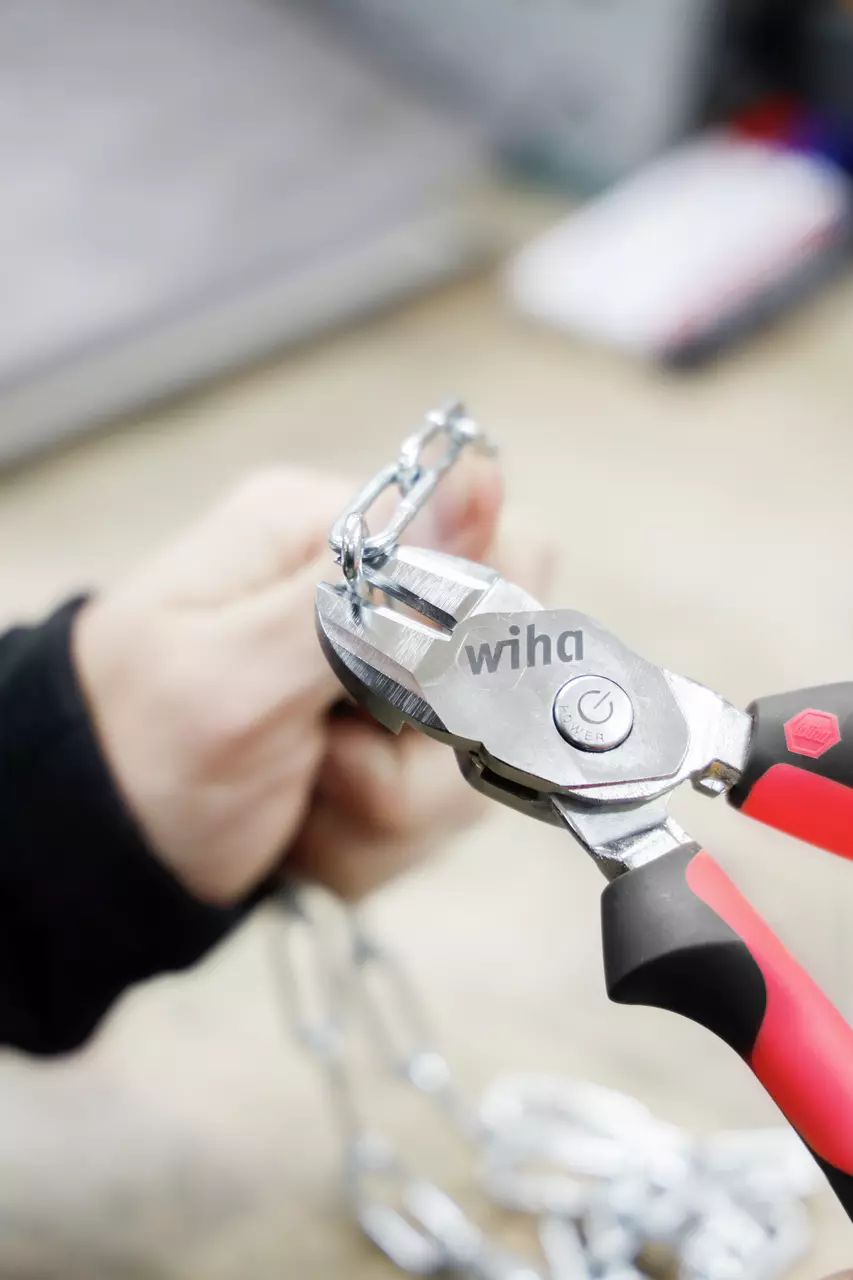 A person using a red-handled cutting plier to cut a metal chain.