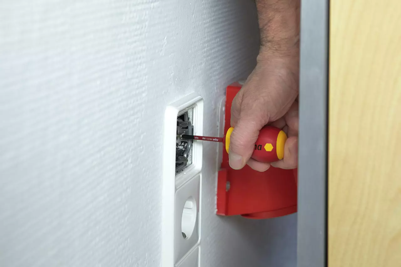 Person using a red and yellow stubby screwdriver on a wall socket