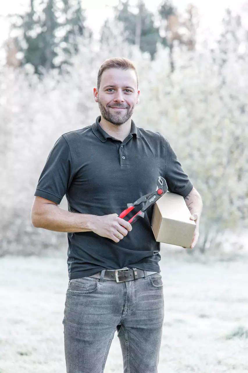 A person holding pliers and a cardboard box outdoors.