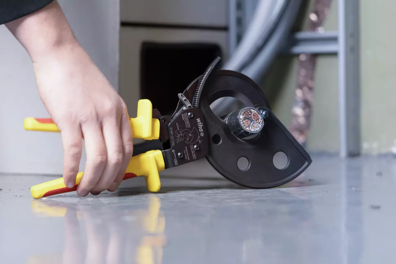 A hand using a ratchet cable cutter on a thick electrical cable