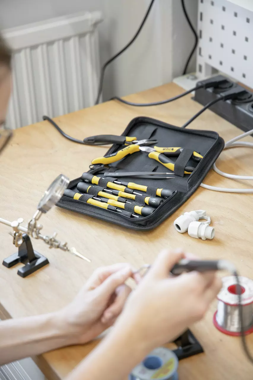 A tool set with yellow-handled tools on a wooden desk, person working with electronics.