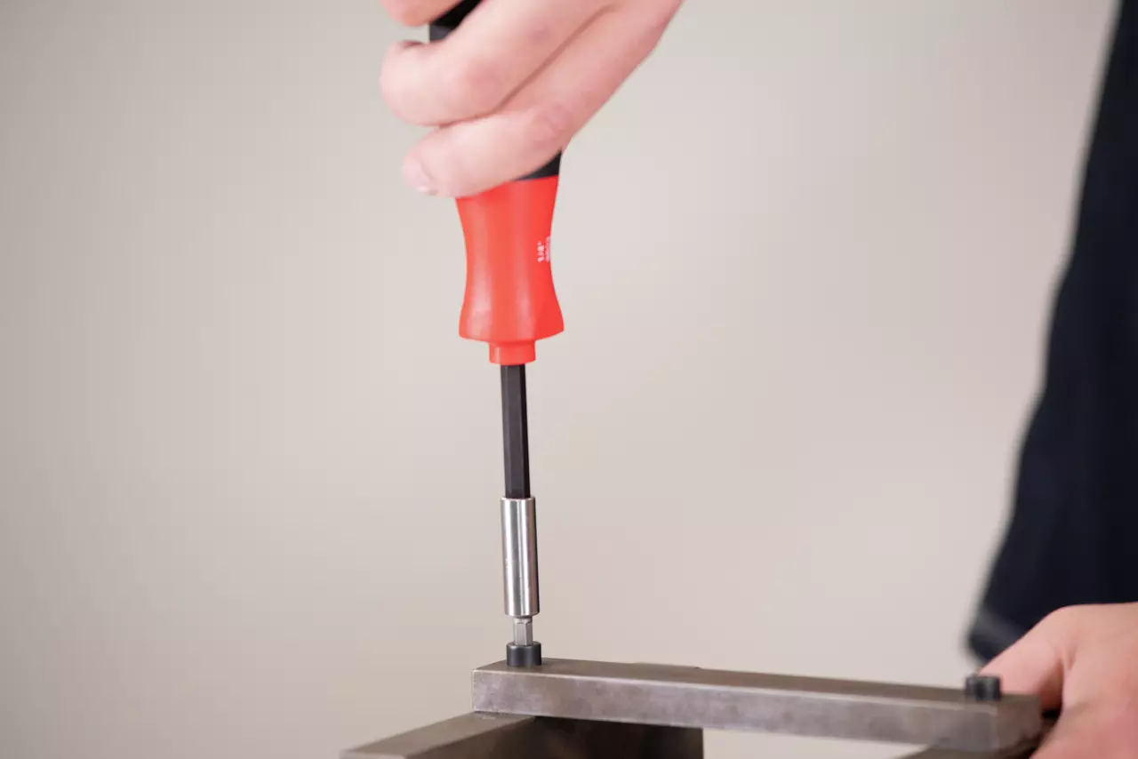 Person using a red-handled screwdriver on a metal piece.