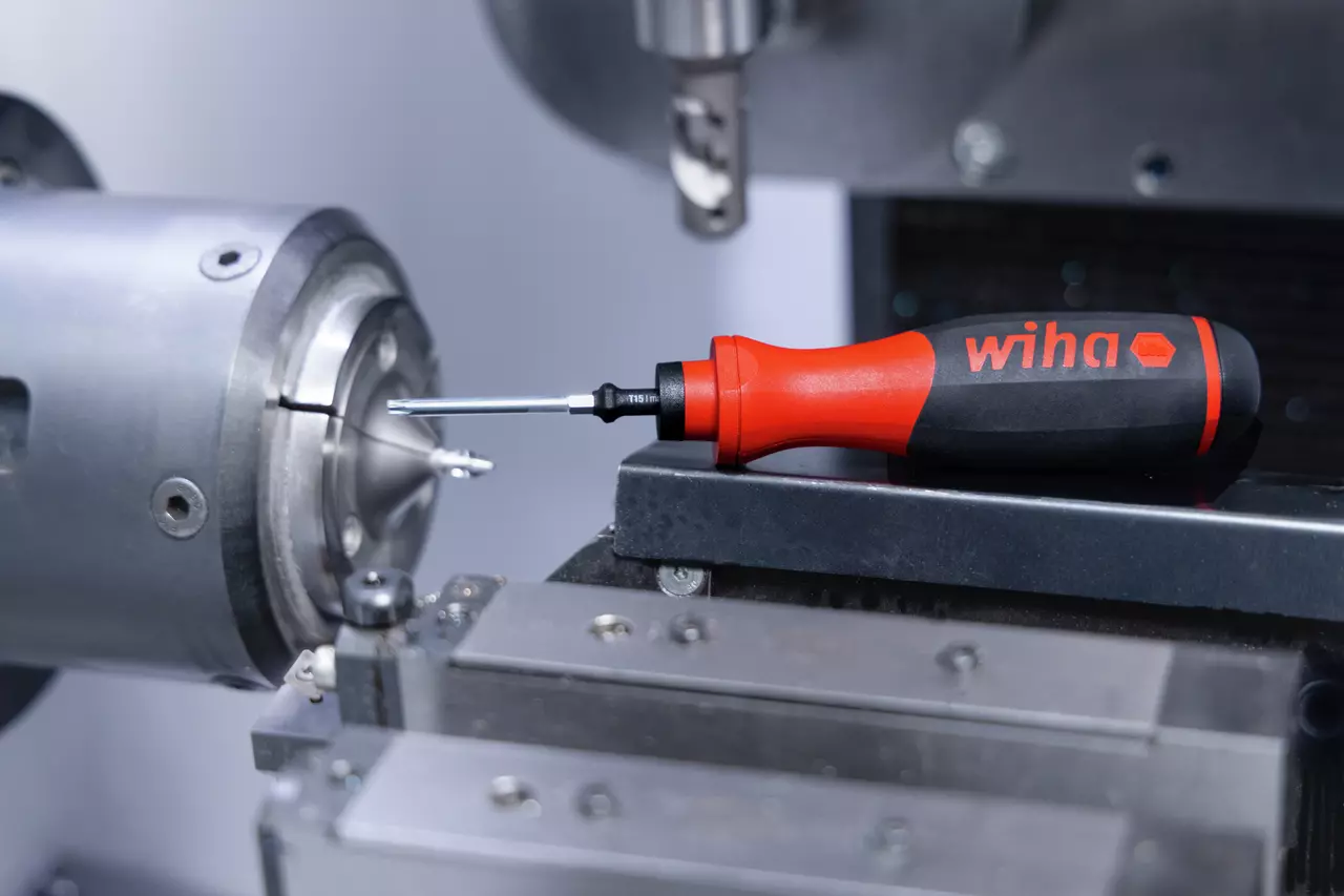 Red and black torque screwdriver next to a metal component in a workshop.