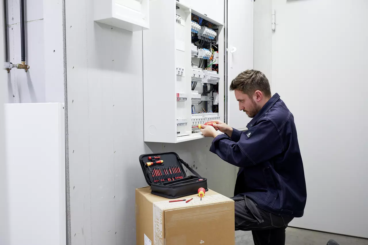 A person working on an electrical panel with tools on a box nearby.
