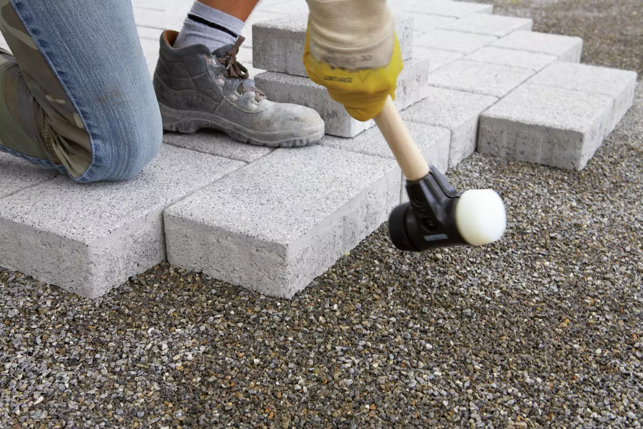 Person using a rubber mallet to lay paving stones on gravel