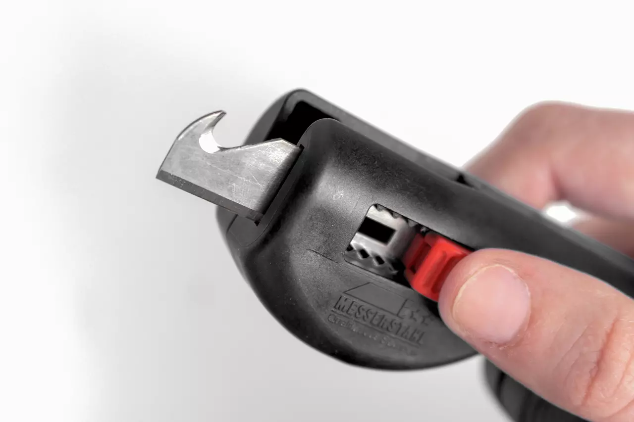 Multifunctional stripping tool with black handle and red slider, held in hand.