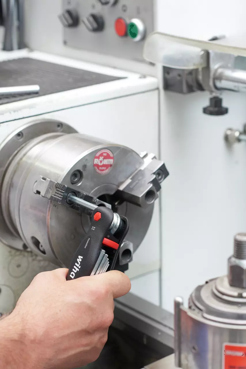 A person using a multi-tool to adjust a metal chuck on a lathe machine.