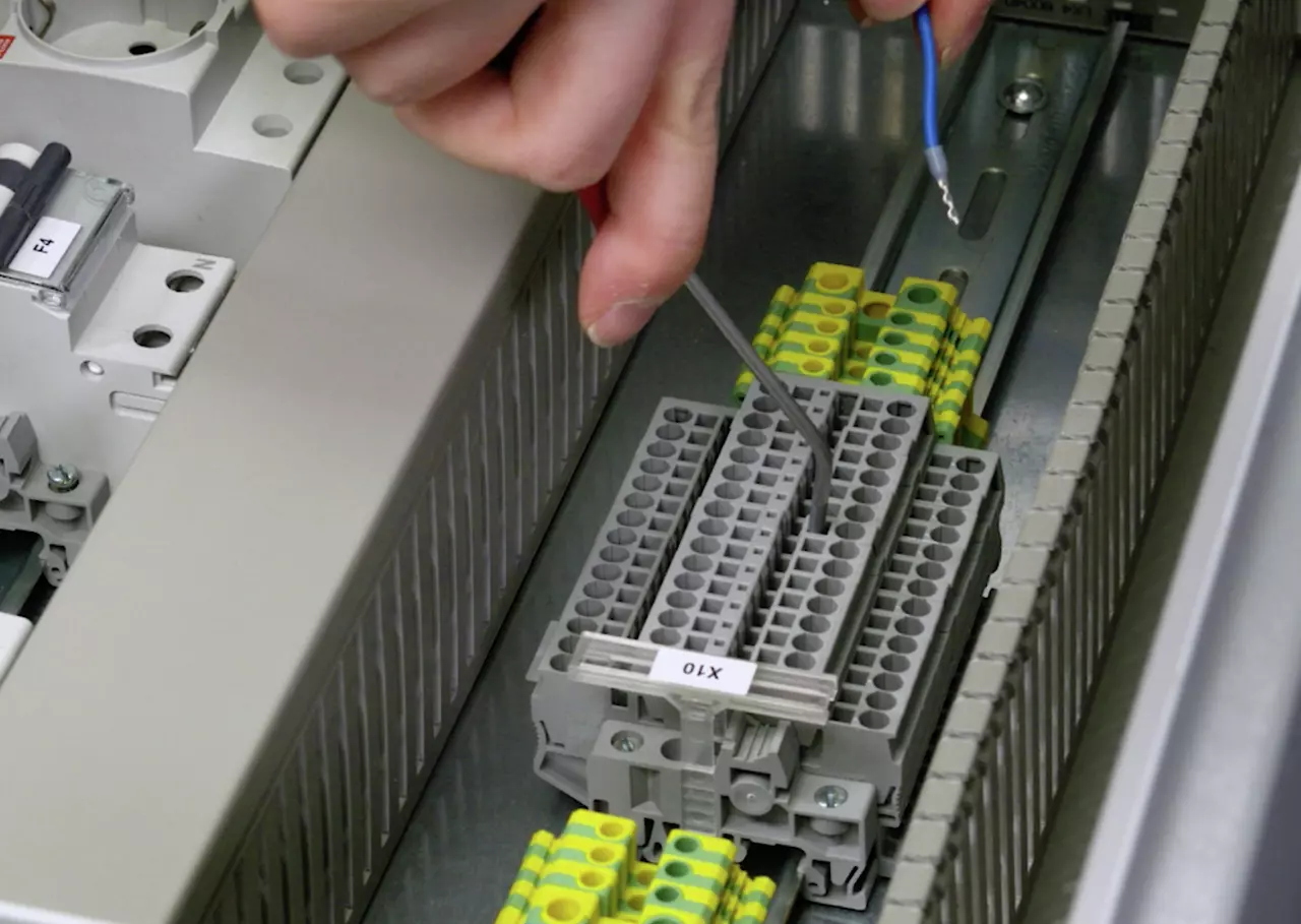 A person uses a tool to adjust a terminal block with gray and yellow connectors in an electrical panel.