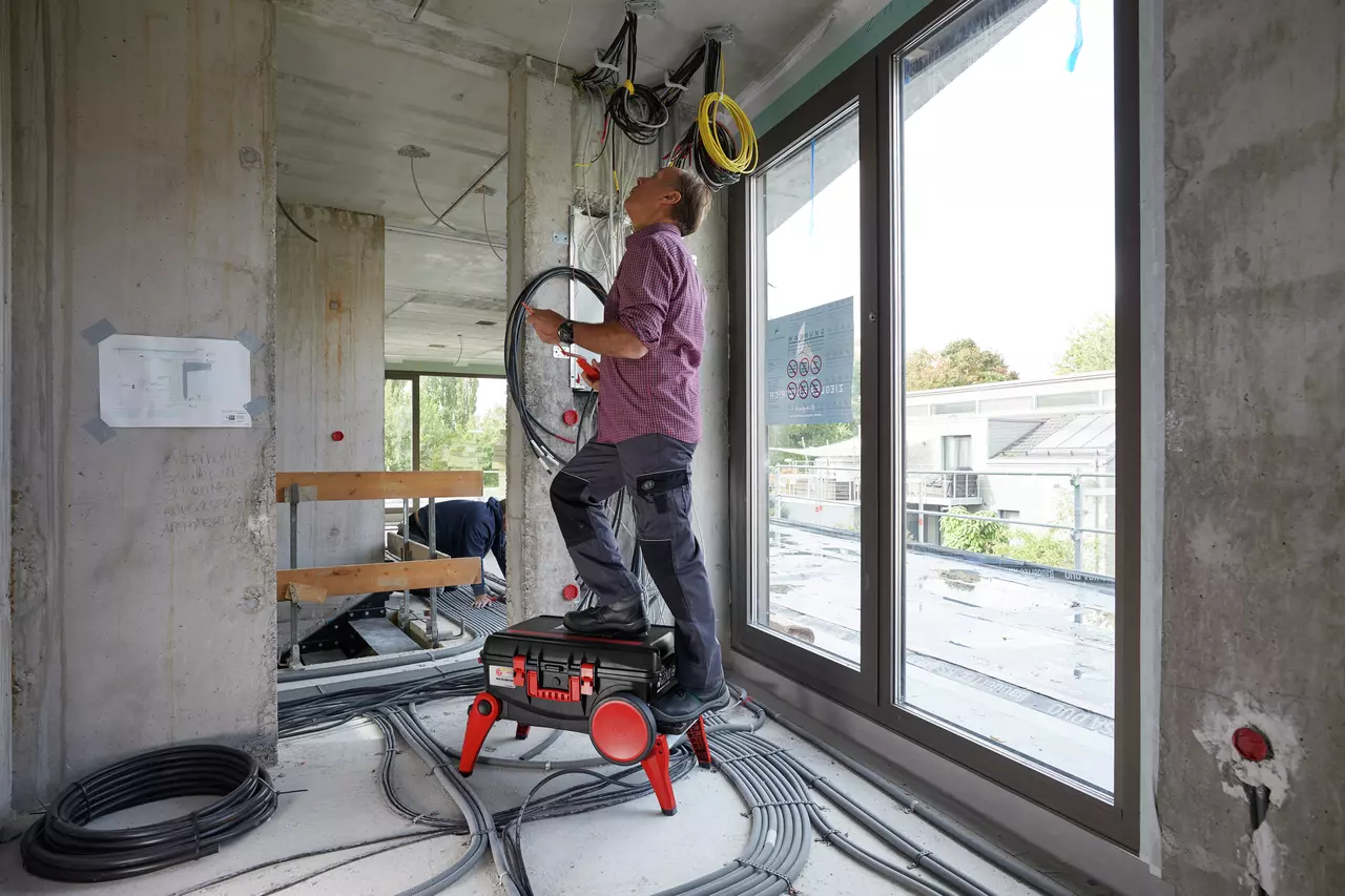 A person standing on a toolbox, working with cables in a construction site.