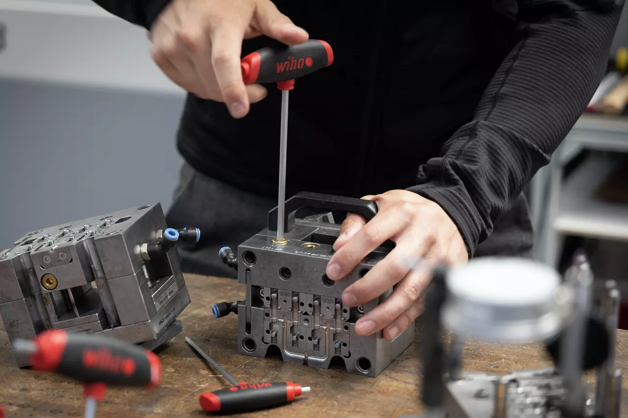 A person is using a T-handle screwdriver on a metal workpiece on a workbench.