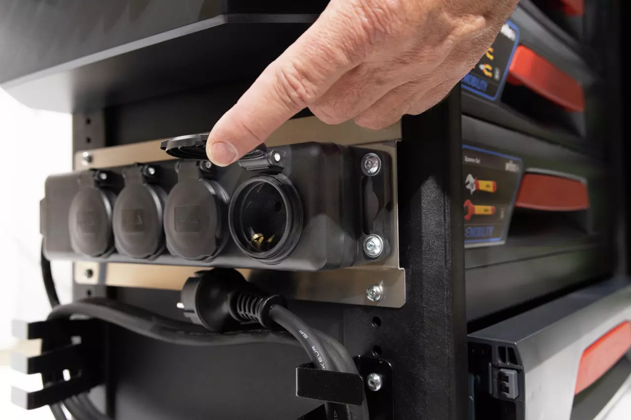 Hand opening a socket cover on a power strip mounted on a trolley