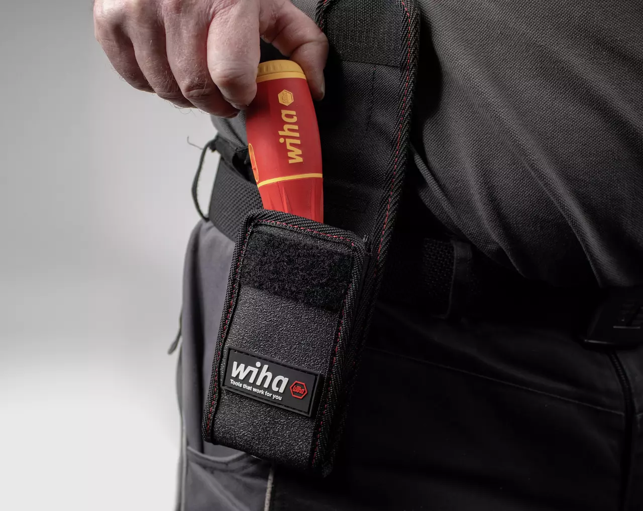 Person placing a red and yellow electric screwdriver into a black belt pouch.