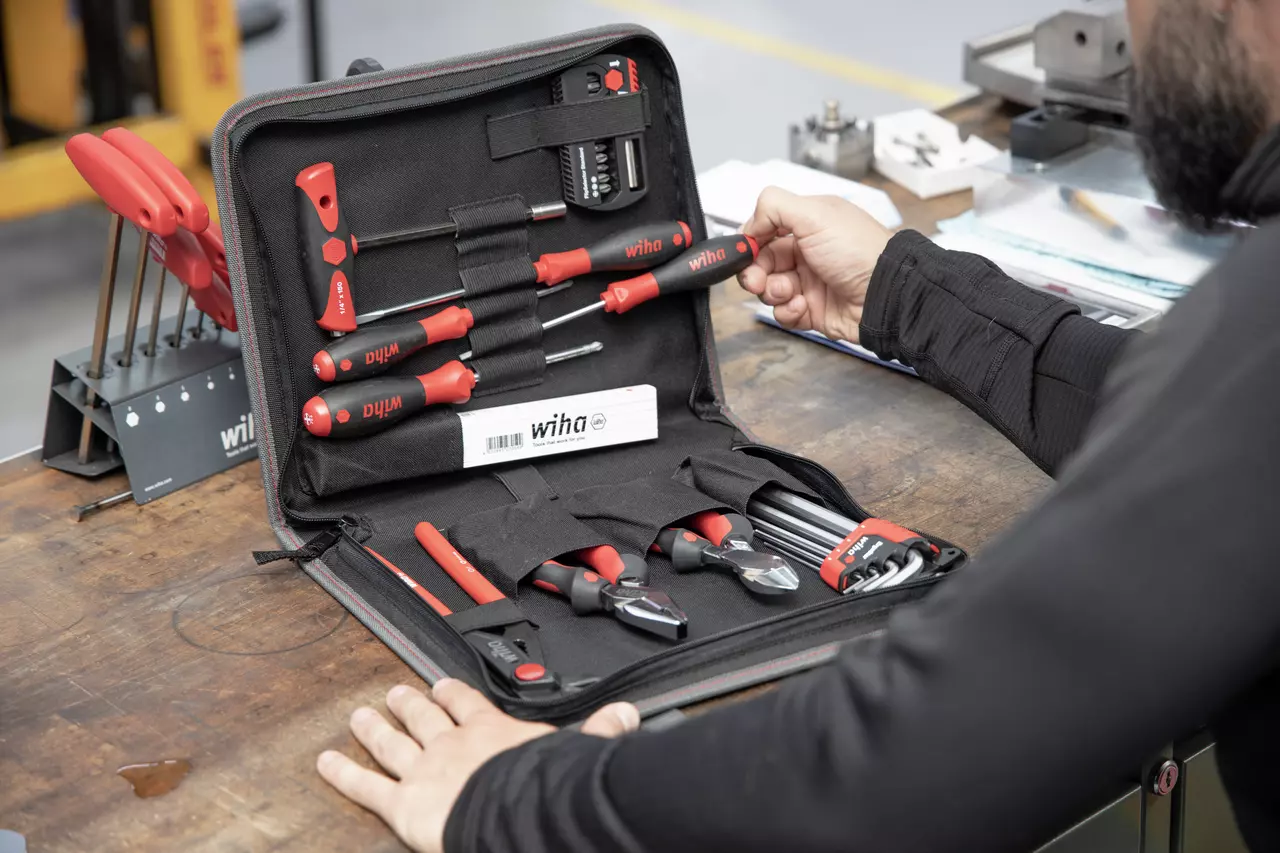 Tool set with screwdrivers and pliers in a black case on a workbench, person holding a screwdriver.