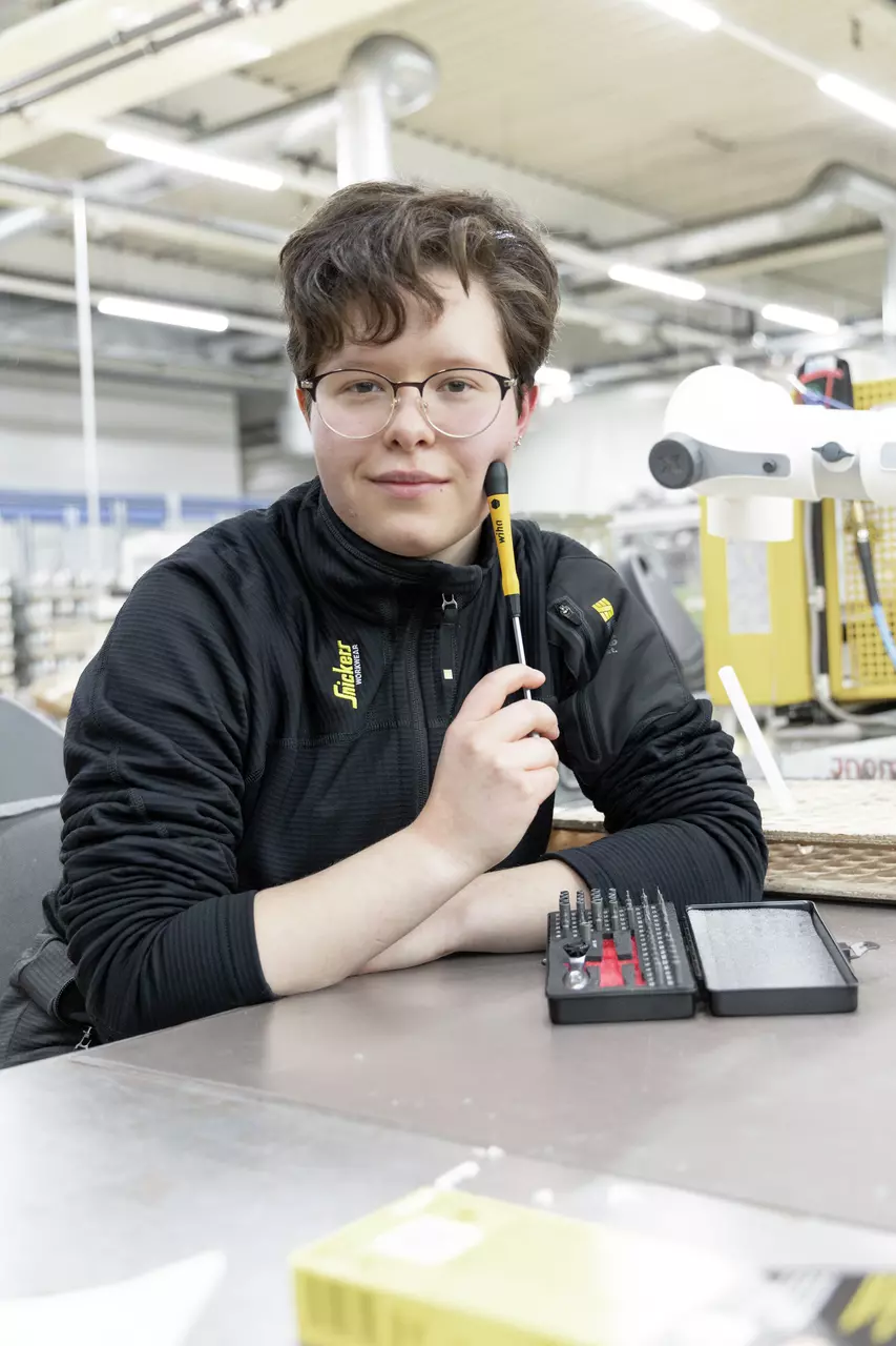 Person with glasses holding a screwdriver in a workshop, in front of a box with screwdriver bits.