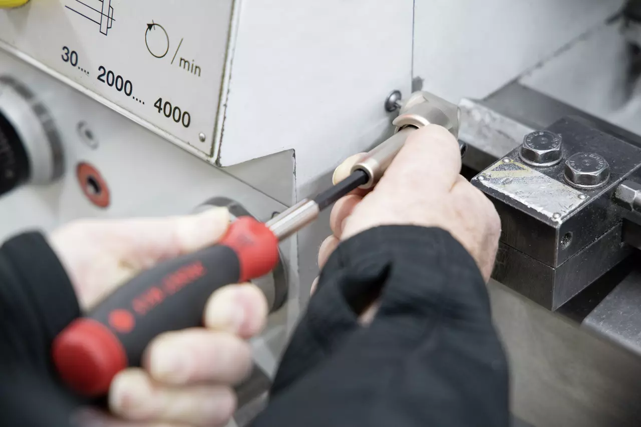 Person using a screwdriver on a metal machine panel