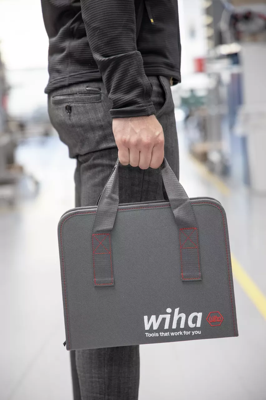 A person holding a gray tool case with red stitching and a logo
