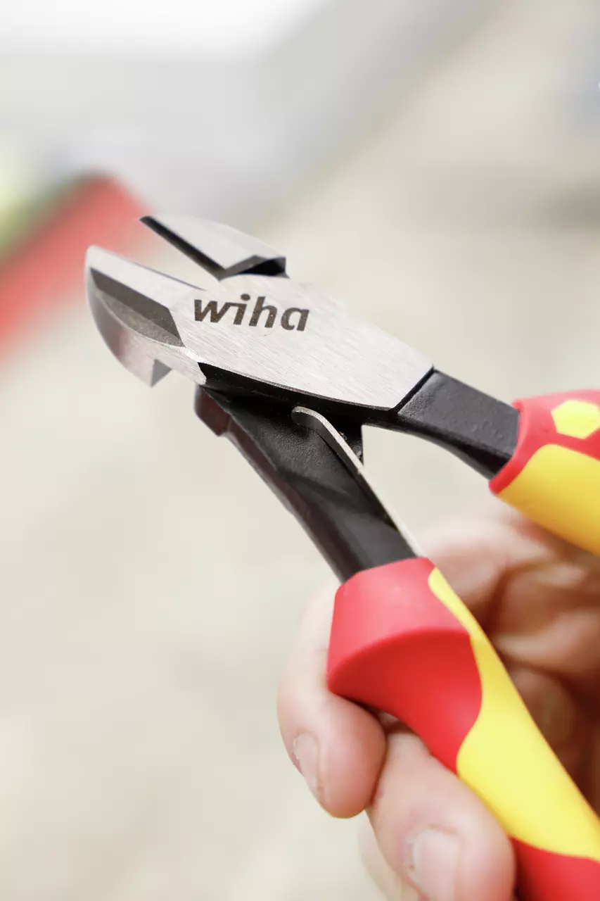 A hand holding red and yellow-handled side cutters with "wiha" branding.