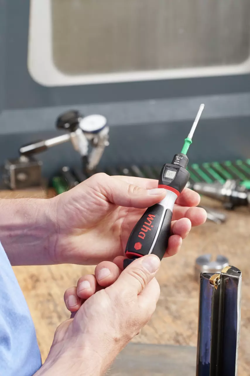 Person holding a torque screwdriver with digital display and black handle in a workshop