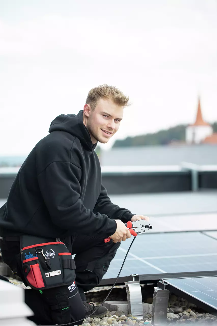 En person bruger et crimpeværktøj på solpaneler udendørs.