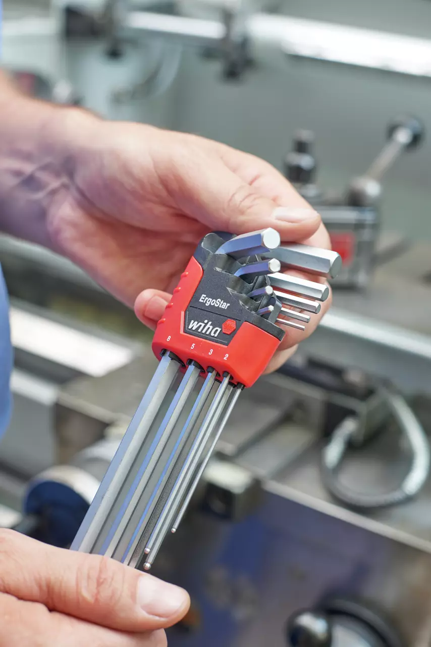 A person holds an ErgoStar hex key set with a red holder in a workshop.