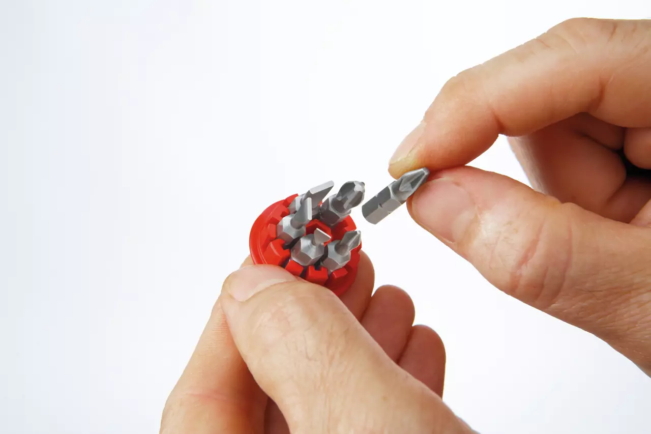 Hands holding a red bit holder with several metal bits, one being removed.