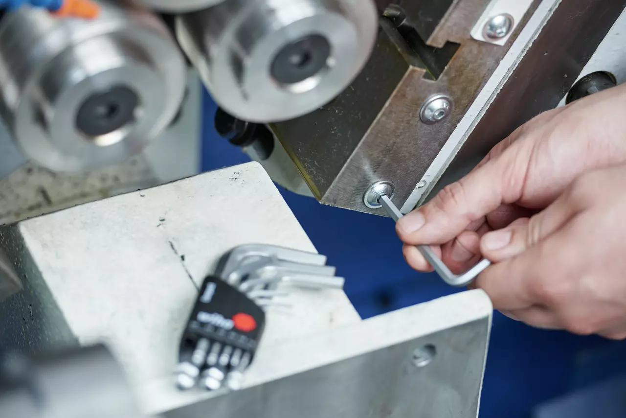 Person using a hex key on a metallic machine part.
