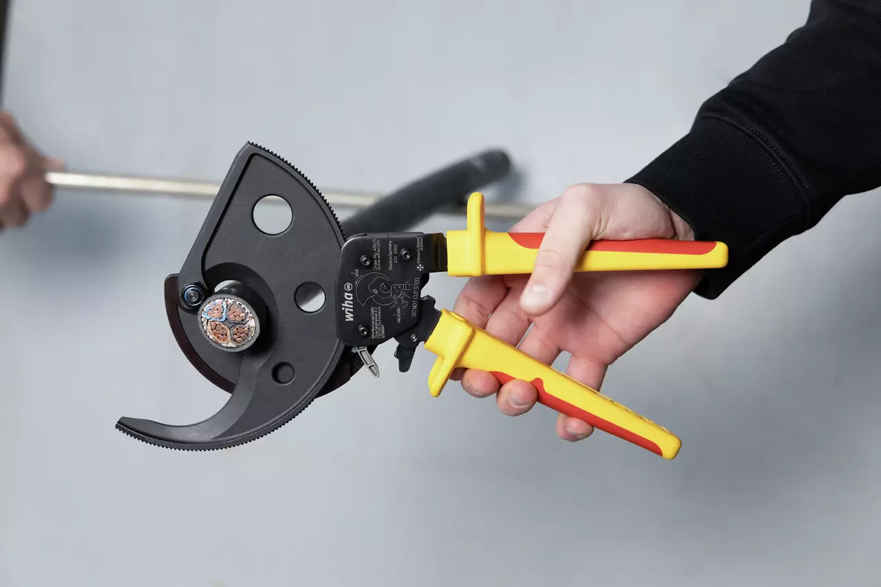 A person holding a ratchet cable cutter with yellow and red handles.