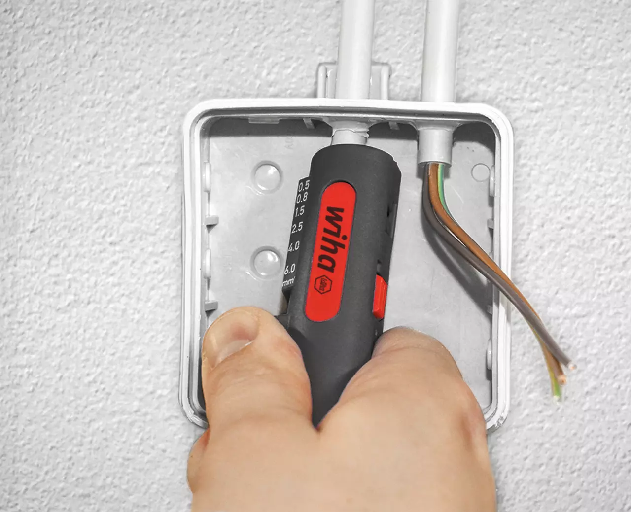 Person using a tool to strip cables in a junction box.