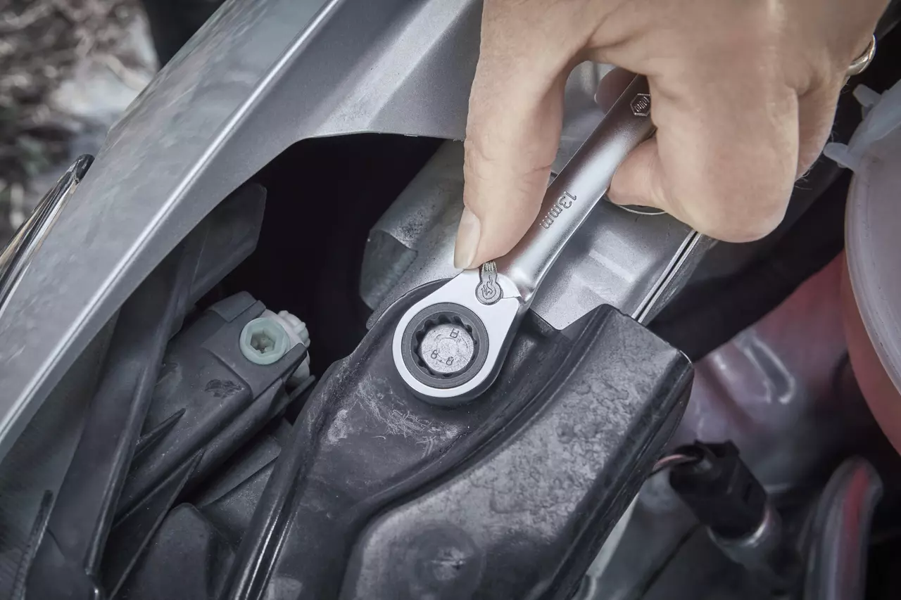 A hand using a ratchet wrench on a bolt in an engine bay.