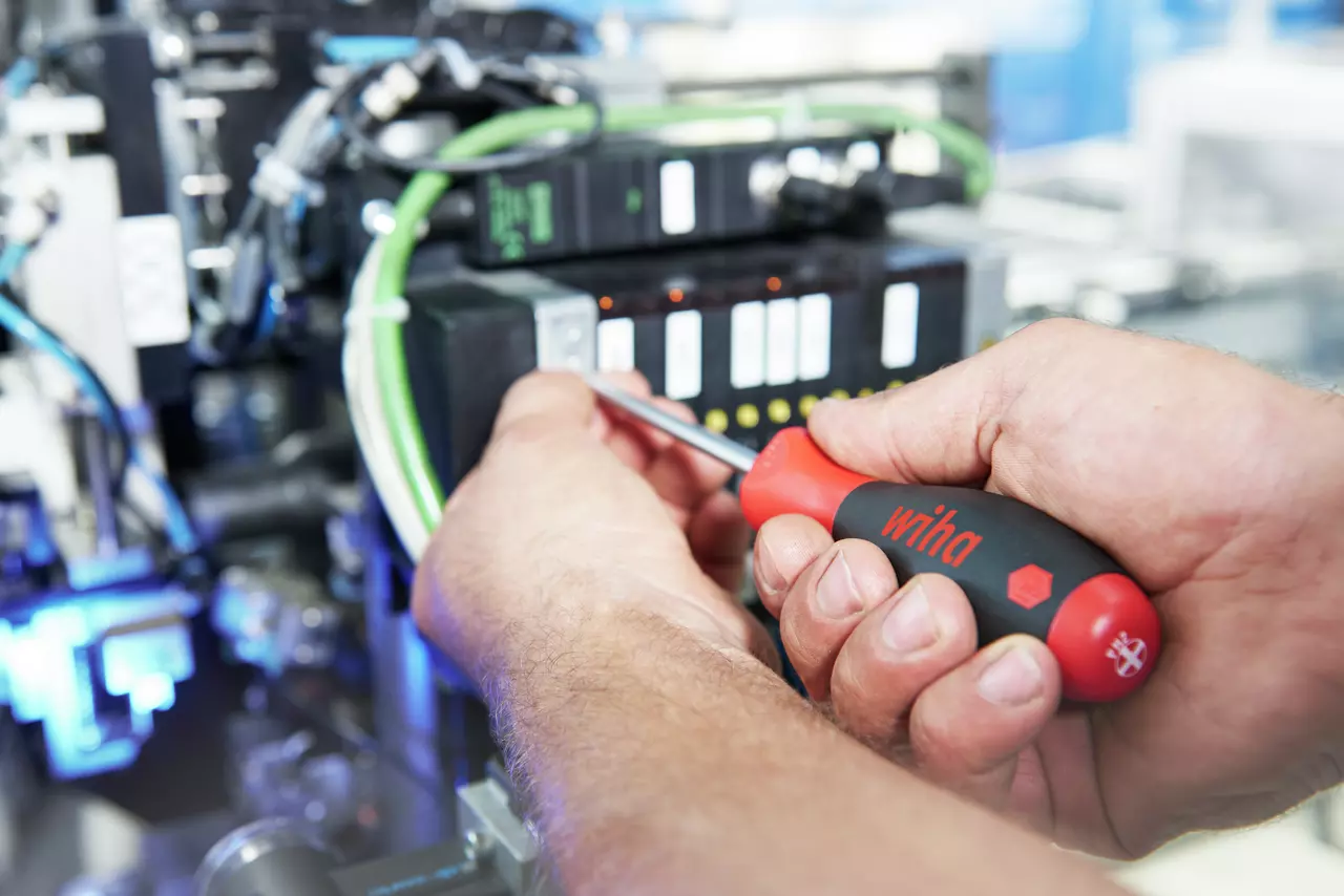 Person using a red and black screwdriver on electronic equipment.