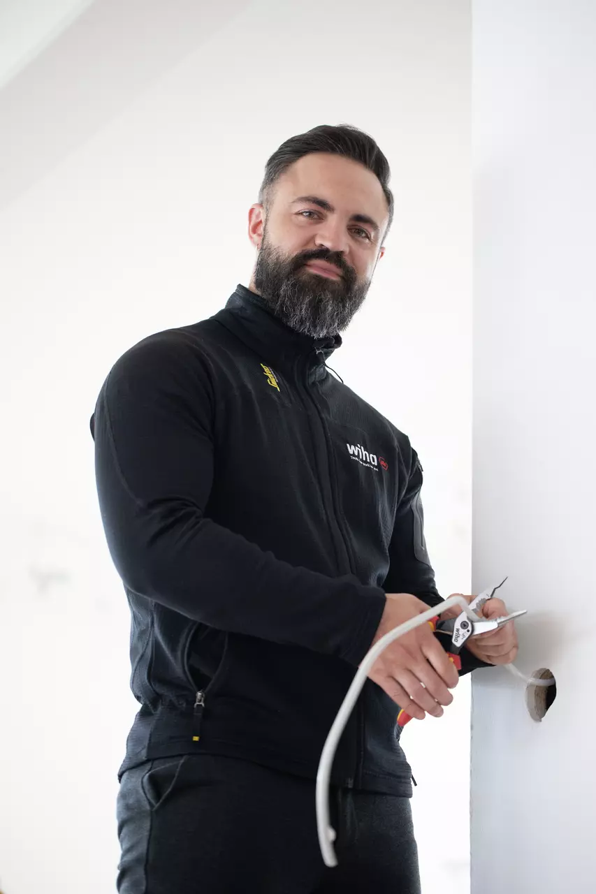 Man in zwarte jas werkt met een tang aan een kabel
