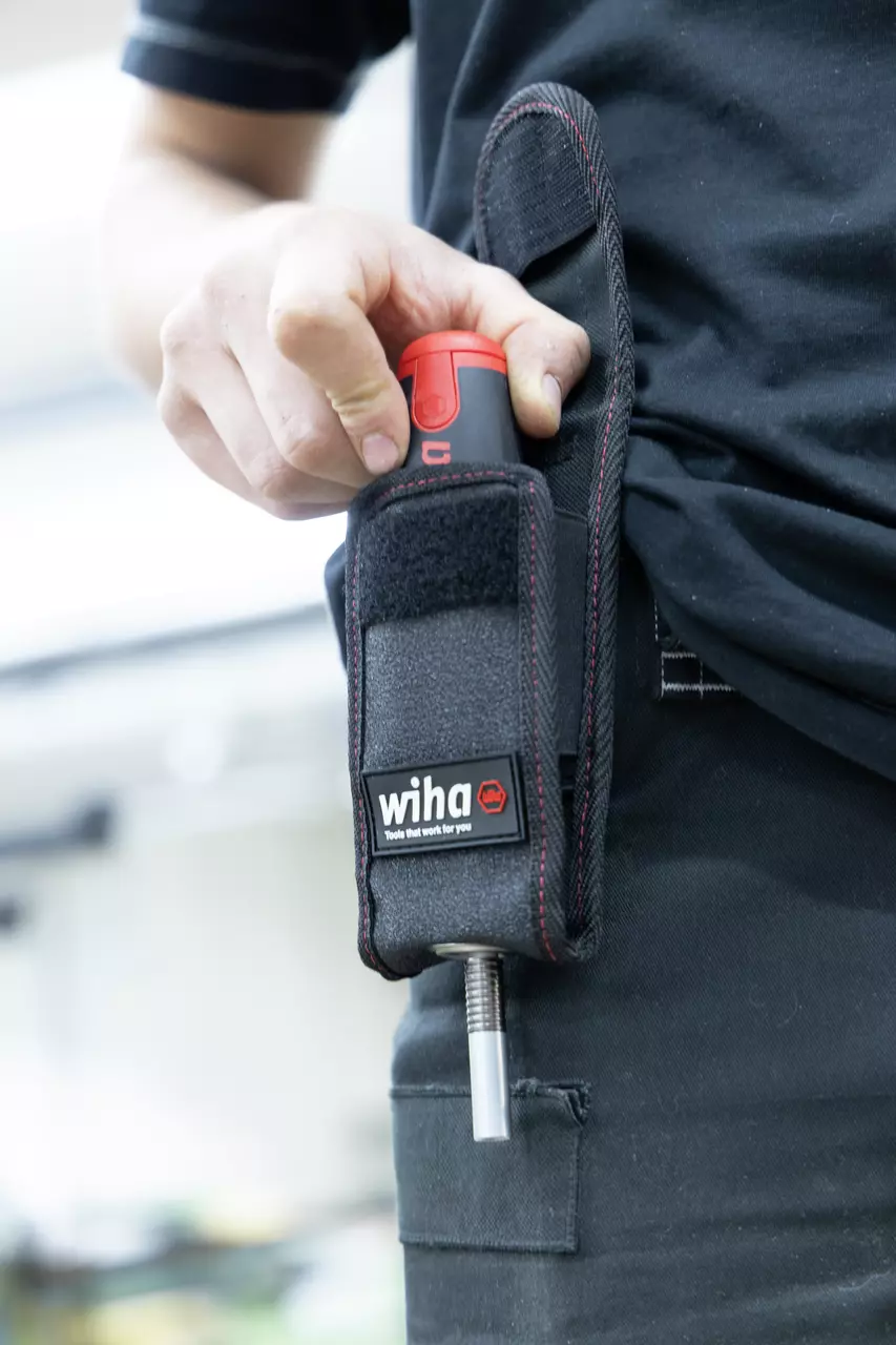 Person placing tool into black belt pouch with red accents